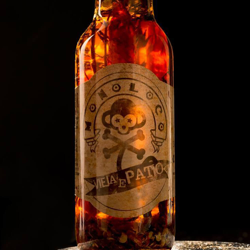 Dramatically backlit bottle of MONOLOCO Vieja’e Patio, showcasing spicy olive oil infused with dried Cayenne peppers and herbs, 150ml.