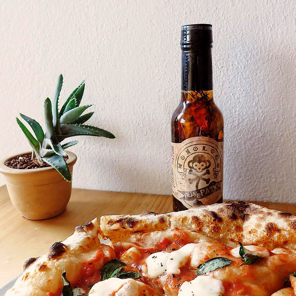 MONOLOCO Vieja’e Patio Hot Sauce, spicy olive oil next to a pizza, showcasing a versatile culinary use with medium heat, 150ml.